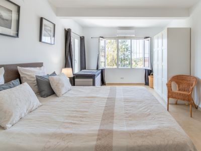 Ruime slaapkamer met groot bed, lichte tegelvloer, witte kledingkast en raam met tralies dat uitkijkt op groen, voorzien van airconditioning.