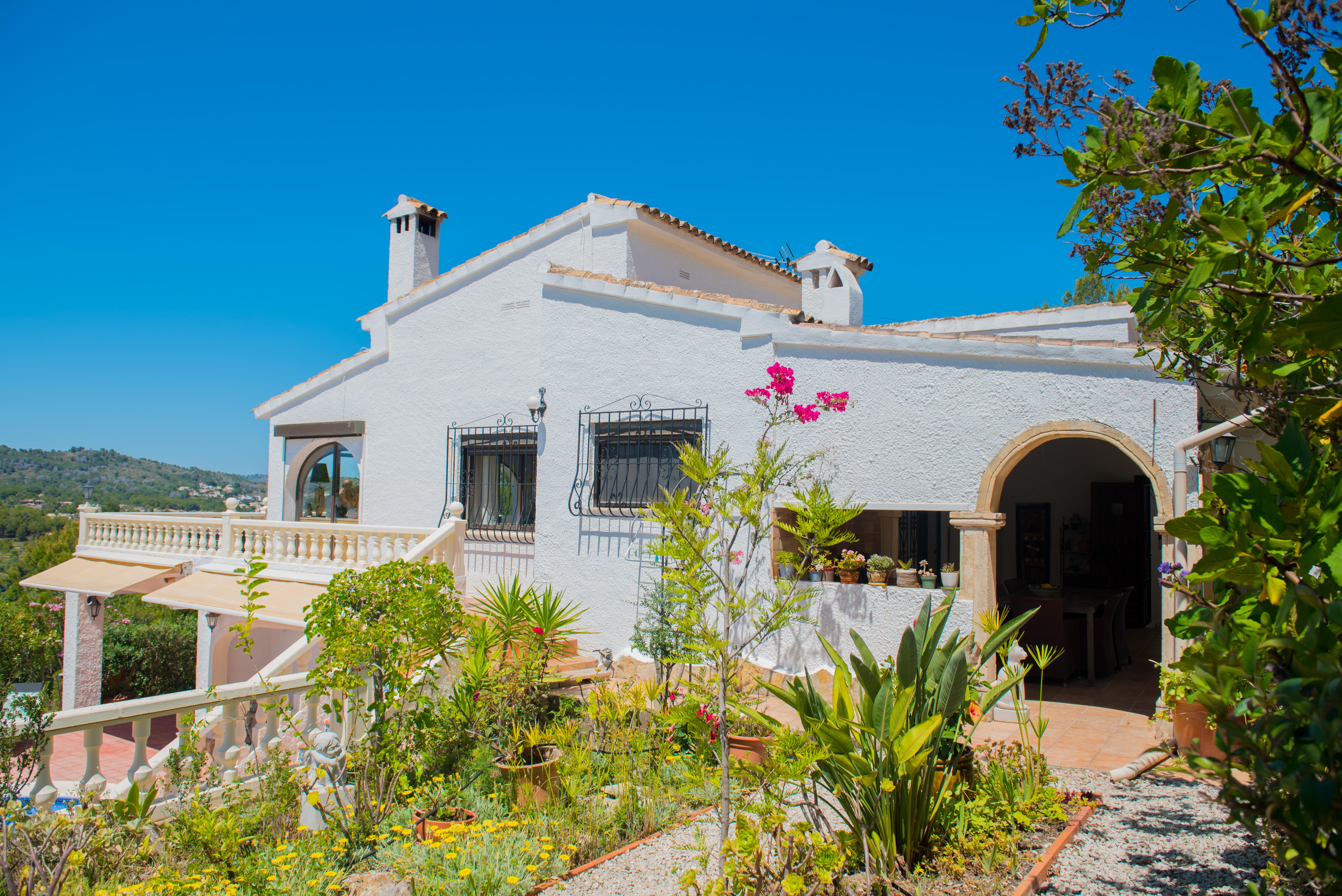 Buitenaanzicht van de mediterrane villa met tuin, getextureerde witte muren en balustrade balkons.