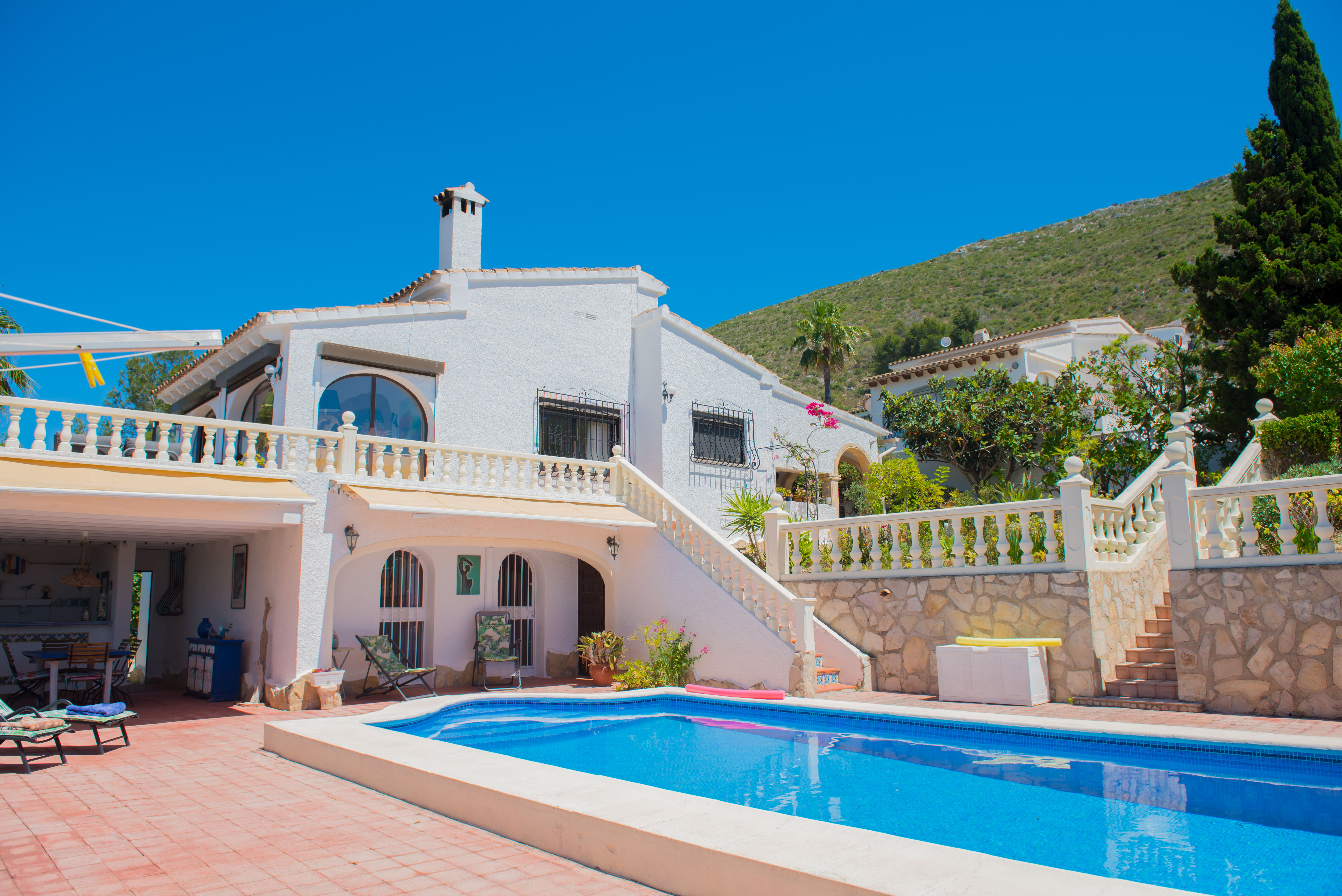 Zwembadzicht met rode tegels en wit huis in mediterrane stijl met stenen trap.