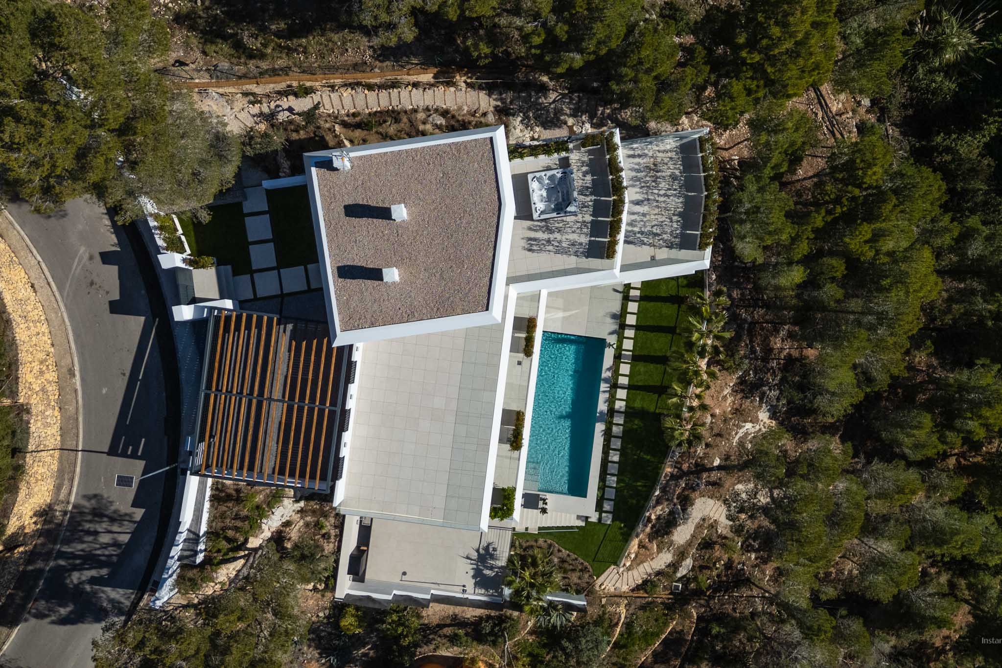 Luchtfoto van de moderne villa met rechthoekig zwembad, ruime betegelde terrassen en een buitenjacuzzi, omgeven door weelderige mediterrane beplanting.