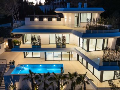 De meerlaagse moderne architectuur van de villa licht op in de schemering, met een levendig blauw zwembad en ruime terrassen met glazen balustrades.