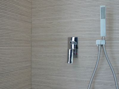 Douchehoek met chromen mengkraan en handdouche tegen een wand bekleed met horizontaal geribbelde textuurtegels.