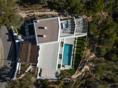 Luchtfoto van de moderne villa met rechthoekig zwembad, ruime betegelde terrassen en een buitenjacuzzi, omgeven door weelderige mediterrane beplanting.