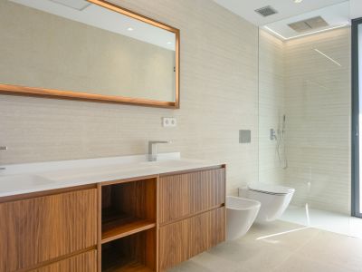 Moderne badkamer met dubbele wastafel, houten meubel en getextureerde wandtegels. Verlichte spiegel, inloopdouche, wandcloset en bidet zijn aanwezig.