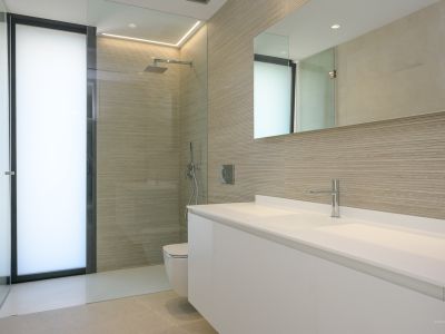 Moderne badkamer met dubbele zwevende witte wastafel, inloopdouche met getextureerde wandtegels en een matglazen deur, aangevuld met chromen kranen en geïntegreerde verlichting.