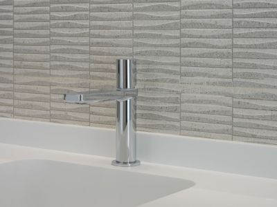 Moderne chromen kraan op een wit werkblad met geïntegreerde wastafel. De achterwand is voorzien van getextureerde lichtgekleurde tegels met een subtiel golfpatroon.