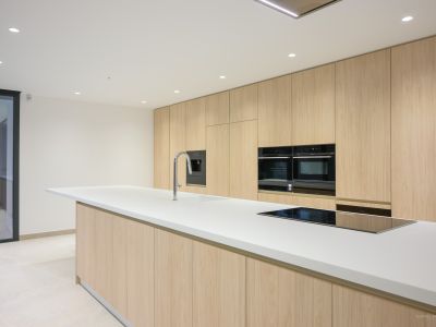 Moderne keuken met een groot wit eiland inclusief geïntegreerde spoelbak en inductiekookplaat, aangevuld met plafondhoge licht houten kasten en inbouwovens.