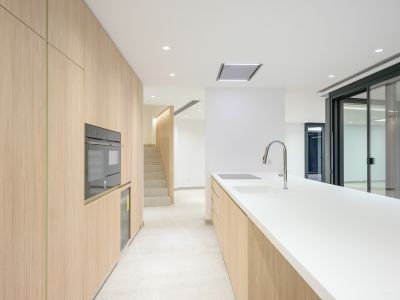 Moderne keuken met lichte houten kasten, wit werkblad en geïntegreerde apparatuur zoals een oven, inductiekookplaat en spoelbak met chromen kraan. Verbonden met trap en buitentoegang.