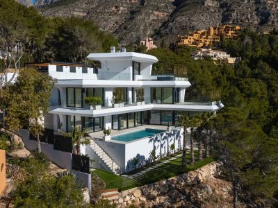 Moderne villa met meerdere verdiepingen, een geïntegreerd rechthoekig zwembad en glazen terrassen, gelegen op een groene heuvel met uitzicht op de bergen.