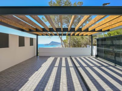 Ruime buitenruimte met pergola van houten balken en metalen frame op kasseien bestrating. Geniet van panoramisch zee- en bergzicht, met scherpe schaduwen van het natuurlijke licht.