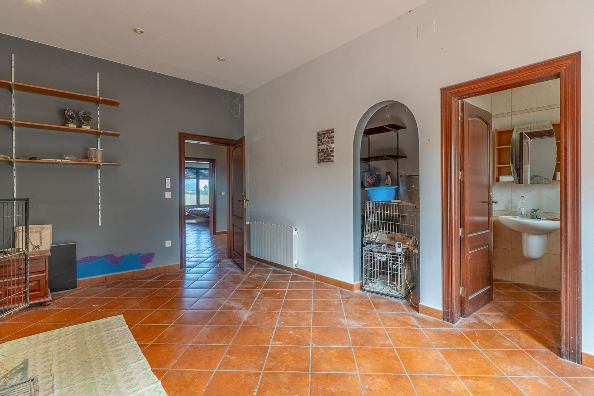 Binnenruimte met terracotta vloertegels, tweekleurige muren en houten deuren. Het beschikt over een gewelfde nis met planken en biedt toegang tot een badkamer en een andere kamer.