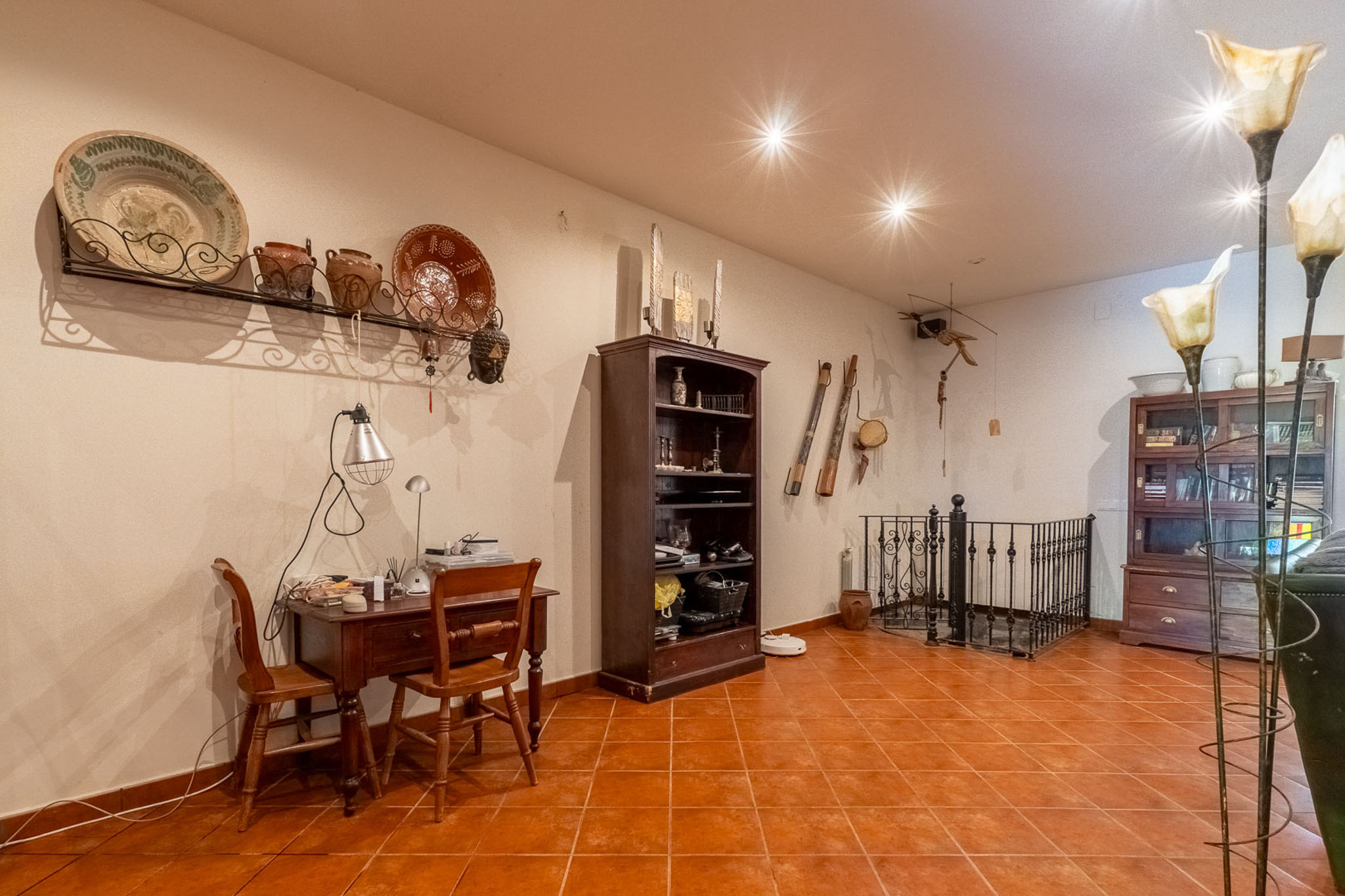 Functionele studeerhoek met houten bureau, terracotta vloertegels en traditionele wanddecoratie. De ruimte omvat een boekenkast en een elegant smeedijzeren balustrade.