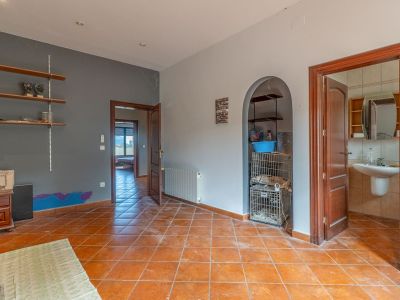 Binnenruimte met terracotta vloertegels, tweekleurige muren en houten deuren. Het beschikt over een gewelfde nis met planken en biedt toegang tot een badkamer en een andere kamer.