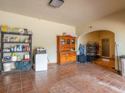 Functionele bijkeuken en opslagruimte in de kelder met terracottategels, wasmachine en opbergrekken, verbonden via een boogdoorgang.