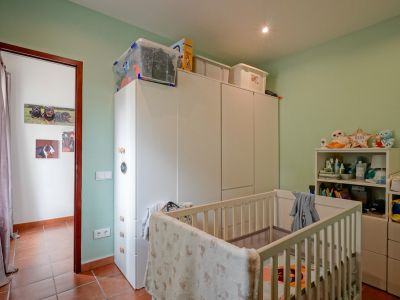 Kinderkamer met lichtgroene muren en terracotta tegelvloer. Voorzien van een wit ledikant, ruime witte kledingkasten en een open rek, verlicht door een inbouwspot in het plafond.