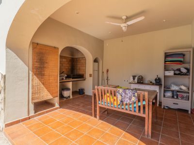 Overdekt terras met terracotta tegels en ingebouwde bakstenen barbecue. Voorzien van een houten eettafelbank, plafondventilator en opbergruimte, ideaal voor buiten dineren.
