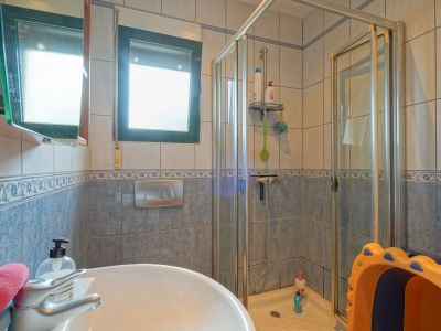 Praktische badkamer met keramische wastafel, glazen douchecabine en blauw-beige tegels. Een raam zorgt voor natuurlijke lichtinval.
