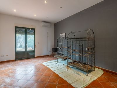 Ruime kamer met terracotta tegels, tweekleurige muren, inbouwverlichting en airconditioning. Dubbele beglazing deur met rolluik en grote metalen vogelkooien zijn zichtbaar.