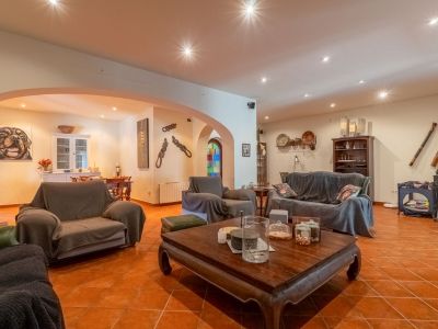 Ruime woonkamer met terracotta tegelvloer en inbouwspots in het plafond. Voorzien van een grote bank, fauteuils en een gesneden houten salontafel, verbonden met een eetruimte via bogen.