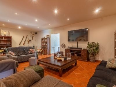 Ruime woonkamer met terracotta vloertegels, inbouwspots in het plafond en een grote wand-tv. Ingericht met donkerhouten meubels en bedekte banken, wat een warme sfeer creëert.