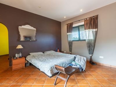 Slaapkamer met tweepersoonsbed, terracotta tegelvloer en tweekleurige muren. Het raam met rolluik en gordijnen biedt natuurlijk licht.