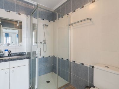 Badkamer met een donker gespikkelde granieten wastafelblad, een decoratieve spiegel en een glazen douchecabine. Muren zijn betegeld met lichtbeige en blauwgrijze tegels met een mozaïekrand.