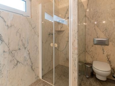 Badkamer met geaderde marmeren wanden en granieten vloer. Voorzien van een glazen douchecabine met geïntegreerde plank en een wandcloset, verlicht door een hooggeplaatst raam.