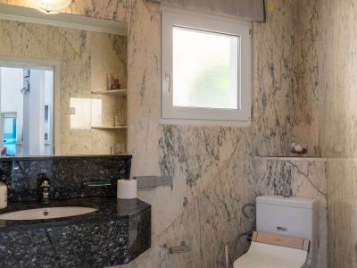 Badkamer met licht geaderde marmeren muren, een donker granieten wastafelmeubel met geïntegreerde wastafel en een grote spiegel. Voorzien van een matglazen raam en toilet met bidetfunctie.