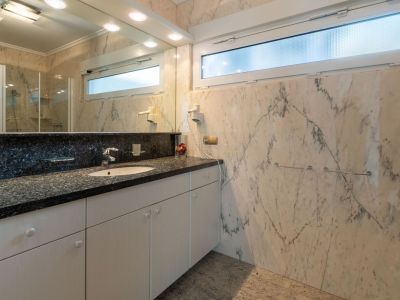 Elegante badkamer met geaderde marmeren wanden en vloer, en een wastafelmeubel met donker granieten blad. Een horizontaal matglazen raam biedt natuurlijk licht en privacy.