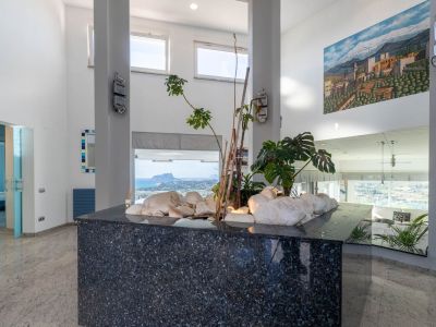 Entreehal met een decoratief eiland van donker graniet, witte stenen en planten. Hoge plafonds en grote ramen bieden panoramisch uitzicht op zee en de Peñón de Ifach.