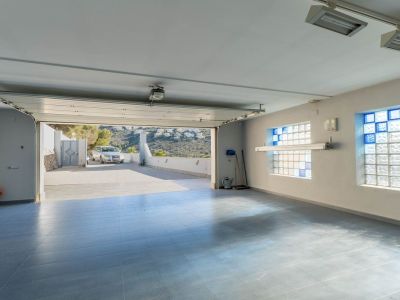 Ruime garage met lichtblauwe tegelvloer en glazen bouwstenen ramen met blauwe accenten, de deur opent naar de oprit en verre heuvels.