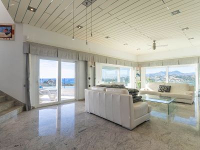 Ruime woonkamer met gepolijste granieten vloeren en lamellenplafonds, met panoramisch uitzicht op zee en bergen en directe toegang tot het terras en zwembad.