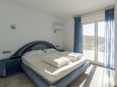 Slaapkamer met blauw designbed en bijpassende nachtkastjes, lichte vloer en directe toegang tot terras via glazen deur, met uitzicht op de heuvel en natuurlijk licht.