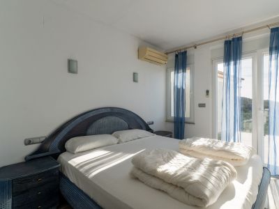 Slaapkamer met blauw-donkerhouten tweepersoonsbed en bijpassende nachtkastjes. Glazen deuren met blauwe gordijnen leiden naar een terras; airconditioning aanwezig.