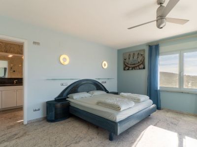 Slaapkamer met een blauwgetint designbed, bijpassende nachtkastjes en lichte marmeren vloer. Het raam biedt heuvelzicht, aangevuld met blauwe gordijnen en een zichtbare en-suite badkamer.
