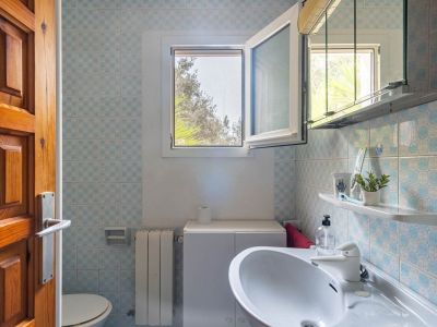 Badkamer met blauw-wit patroon tegels, wastafel met onderkast en open raam dat natuurlijk licht en uitzicht op groen buiten biedt.