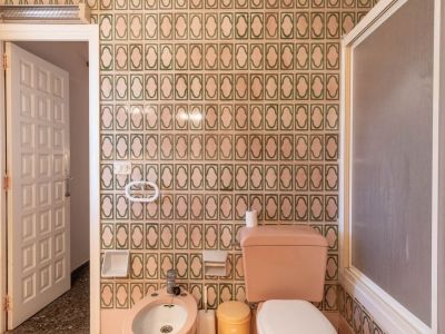 Badkamer met groen-beige patroontegels, roze toilet en bidet, een matte douchewand en een gespikkelde terrazzovloer.