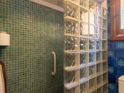 Doucheruimte met groenblauwe mozaïektegels en een glazen bouwstenen wand. Voorzien van een handgreep en een houten raam met gestructureerd glas.