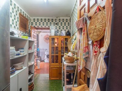 Functionele bijkeuken met patroonbehang, groene tegelvloer, open schappen met keukengerei en een houten vitrinekast. Een wasruimte is achterin zichtbaar.