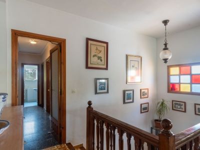 Lichte hal met klassieke houten trap en balustrade. Een opvallend glas-in-loodraam en ingelijste kunstwerken sieren de witte muur.