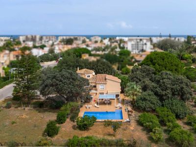 Luchtfoto van de villa met blauw zwembad, een schaduwrijk terras en een ruime, groene tuin. Op de achtergrond zijn de stad en de Middellandse Zee zichtbaar.