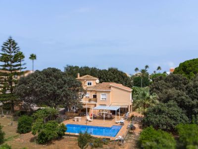 Luchtfoto van de villa met twee verdiepingen en pannendak, met het blauwe zwembad, betegeld terras met pergola en de uitgestrekte mediterrane tuin.