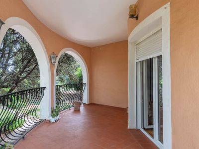 Overdekt terras met terracotta tegels, elegante bogen en smeedijzeren balustrades. Biedt uitzicht op het groen en toegang via een schuifdeur.