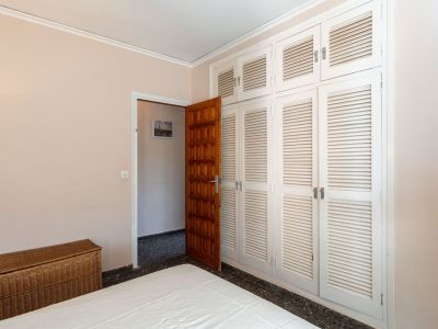 Slaapkamer met een ruime inbouwkast met witte lamellendeuren, een donkere houten toegangsdeur en een bed. Een rieten kist voegt een warme toets toe.