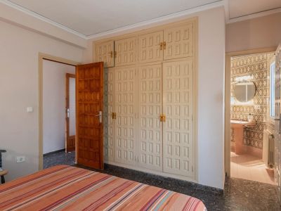 Slaapkamer met ruime, lichtgekleurde inbouwkast met paneeldeuren en donkere terrazzovloer, met directe toegang tot een betegelde badkamer.