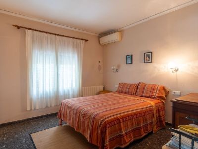 Tweepersoons slaapkamer met gestreept beddengoed, raam met lichte gordijnen, donkere vloer en airconditioning.