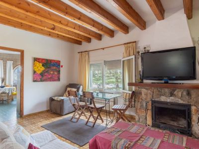 Woonkamer met houten balkenplafond en stenen open haard. Natuurlijk licht valt binnen via het raam, wat zorgt voor een warme sfeer.