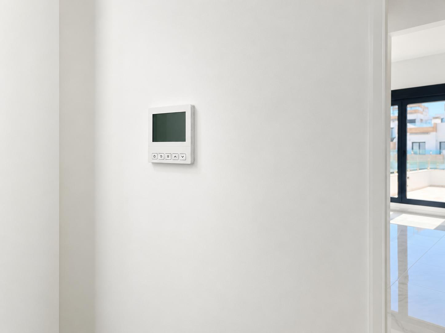Een strak digitaal klimaatregelpaneel is gemonteerd op een smetteloze witte muur, met een doorkijk naar een lichte aangrenzende kamer en buitenterras.