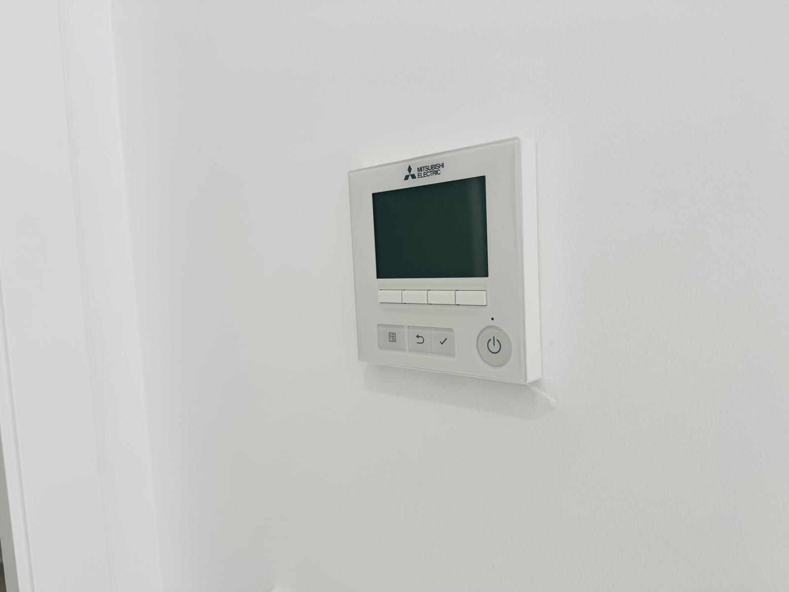 Mitsubishi Electric bedieningspaneel voor kanaalairconditioning, met digitaal display en intuïtieve knoppen, naadloos geïntegreerd in de witte muur.