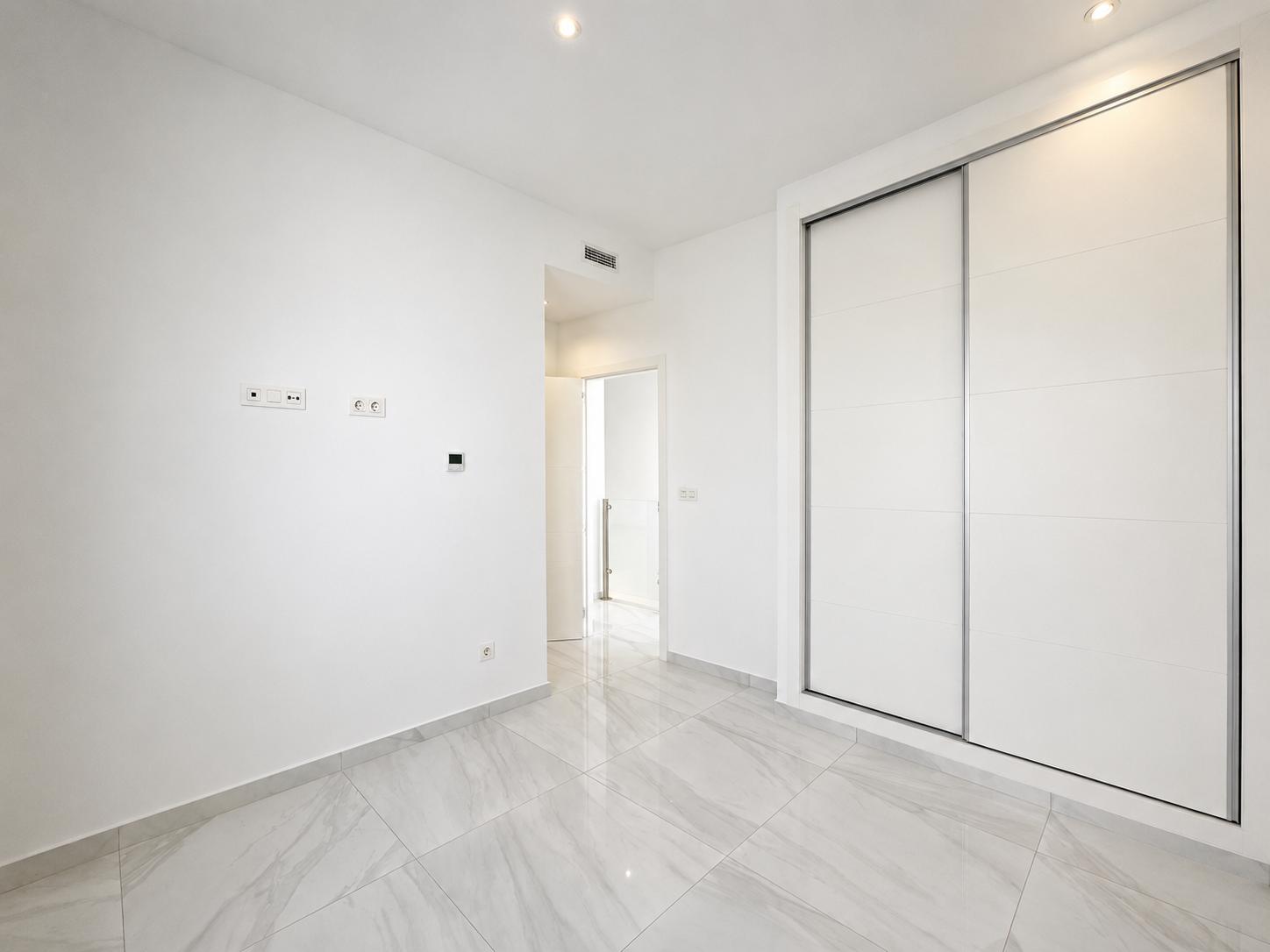 Moderne kamer met grote witte inbouwschuifkasten, lichtgrijze marmerlook vloertegels en inbouwspots. Een strak en functioneel ontwerp.